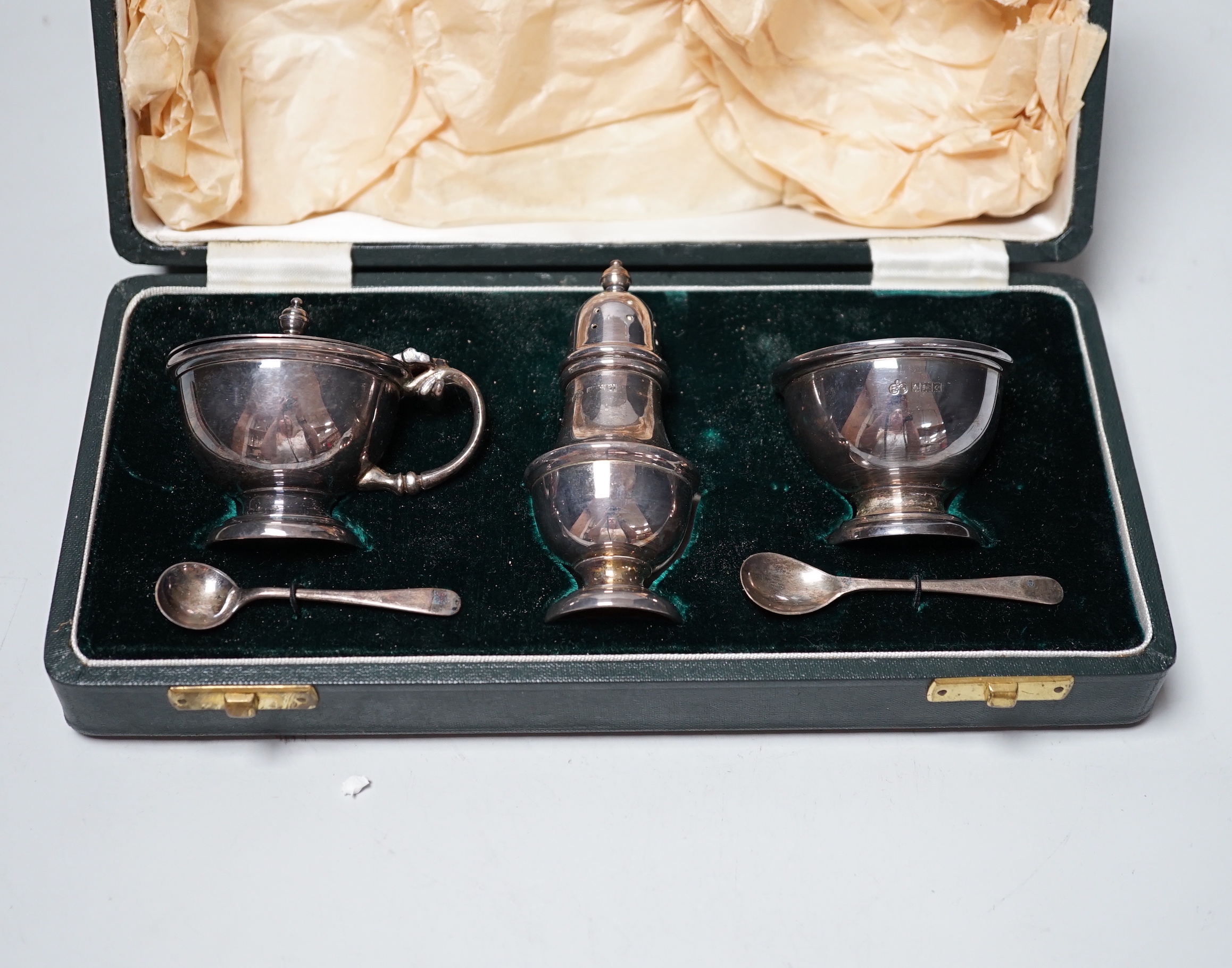 An Elizabeth II cased silver three piece condiment set, Elkington & Co, Birmingham, 1963 and two silver condiment spoons.